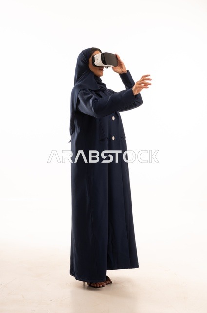 الإشارة باليد لشئ ما تشاهده، بورتريه لإإمرأة عربية خليجية سعودية سعيدة ترتدي نظارة الواقع الإفتراضي ثلاثية الأبعاد الفريدة و العجيبة، التفاعل و المتعة و التسلية بمشاهدة الأفلام و ألعاب العالم الافتراضي ، تقنيات و ألعاب ، خلفية بيضاء