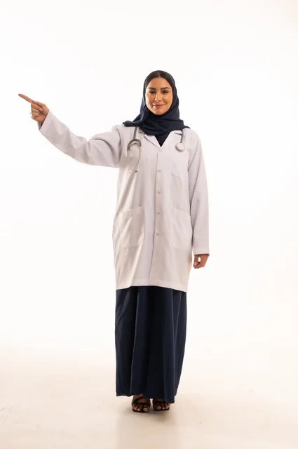 تعابير يد الأتجاه من هذه الجهة ايماءات الثقة بالنفس، الاهتمام بالمظهر الخارجي، تقديم الفحص الطبي والخدمات العلاجية، بورتريه مقرب لطبيبة عربية خليجية سعودية محجبة مبتسمة ترتدي معطف الطبيب وتضع السماعات الطبية، مفهوم الأنوثة والنعومة، خلفية بيضاء