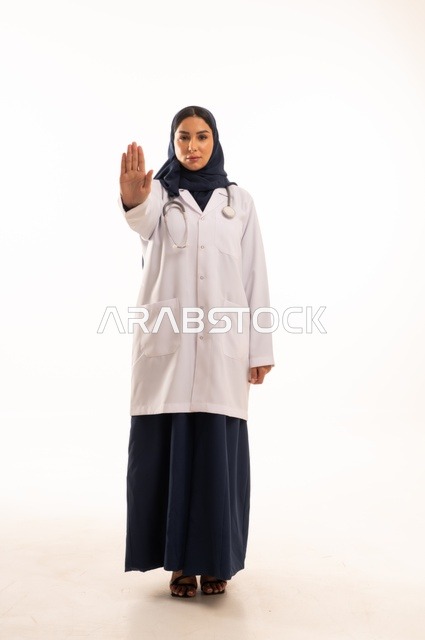 تعابير يد قف النظر إلى الكاميرا بايماءات الثقة بالنفس، الاهتمام بالمظهر الخارجي، تقديم الفحص الطبي والخدمات العلاجية، بورتريه مقرب لطبيبة عربية خليجية سعودية محجبة مبتسمة ترتدي معطف الطبيب وتضع السماعات الطبية، مفهوم الأنوثة والنعومة، خلفية بيضاء