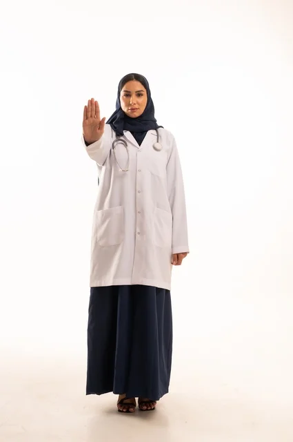 تعابير يد قف النظر إلى الكاميرا بايماءات الثقة بالنفس، الاهتمام بالمظهر الخارجي، تقديم الفحص الطبي والخدمات العلاجية، بورتريه مقرب لطبيبة عربية خليجية سعودية محجبة مبتسمة ترتدي معطف الطبيب وتضع السماعات الطبية، مفهوم الأنوثة والنعومة، خلفية بيضاء