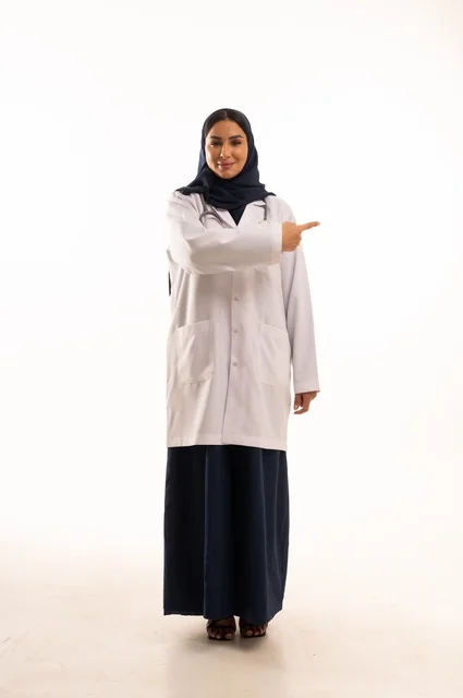 تعابير يد الأتجاه من هذه الجهة ايماءات الثقة بالنفس، الاهتمام بالمظهر الخارجي، تقديم الفحص الطبي والخدمات العلاجية، بورتريه مقرب لطبيبة عربية خليجية سعودية محجبة مبتسمة ترتدي معطف الطبيب وتضع السماعات الطبية، مفهوم الأنوثة والنعومة، خلفية بيضاء