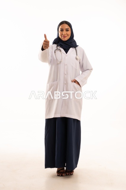 Thumbs up gesture, looking at the camera with self-confidence gestures, attention to appearance, providing medical examinations and treatment services, a close-up portrait of a smiling Saudi Gulf Arab female doctor wearing a doctor's coat and stethoscope, the concept of femininity and softness, white background.