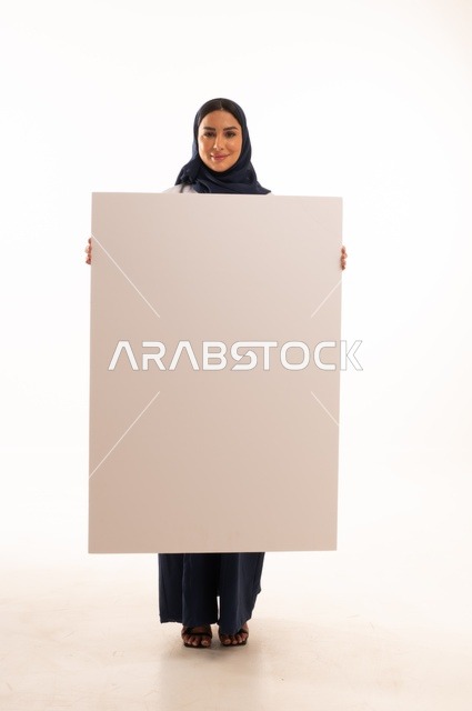Illustrative boards and educational tools, marketing presentations and advertisements, a portrait of an Arab Gulf Saudi female doctor wearing an abaya and a white apron holding a blank rectangular white board in her hands, a young Saudi woman looking at the camera with expressions of determination and seriousness, a white rectangular mockup, white background.