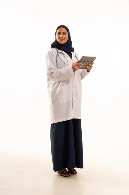 متابعة العمل باستخدام جهاز لوحي، استخدام التقنية الحديثه المتطورة في الحياة العملية، بورتريه لإمرأة عربية خليجية سعودية ترتدي الحجاب والعباءة تقوم بالعمل على التابلت، تصفح مواقع التواصل، صورة الجسم بالطول الكامل، خلفية بيضاء