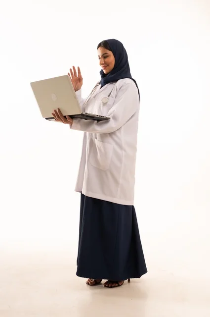 مكالمة فيديو باستخدام التكنولوجيا متابعة العمل، استخدام التقنية الحديثه المتطورة في الحياة العملية، بورتريه لإمرأة عربية خليجية سعودية ترتدي الحجاب والعباءة تقوم بالعمل على الحاسوب المحمول، متابعة وتصفح مواقع التواصل، صورة الجسم بالطول الكامل، خلفية بيضاء