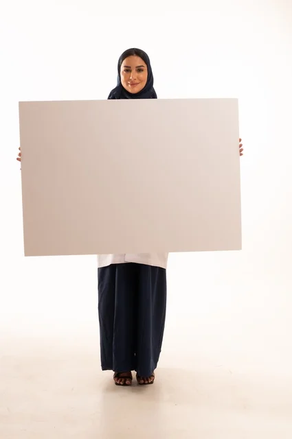 لوحات توضيحية ووسائل تعليمية, العروض والإعلانات التسويقية, بورتريه لطبيبة عربية خليجية سعودية ترتدي العباءة والمئزر الأبيض تمسك بيديها لوحة بيضاء مستطيلة فارغة، شابة سعودية تنظر إلى الكاميرا بتعابير الحزم والجدية، موك اب مستطيل أبيض, خلفية بيضاء