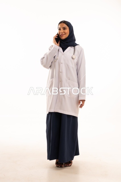 إجراء مكالمة هاتفية باستخدام الأجهزة الحديثة، استخدام التقنية الحديثه المتطورة في الحياة العملية، بورتريه لإمرأة عربية خليجية سعودية ترتدي الحجاب والعباءة تقوم بالعمل على الهاتف المحمول، متابعة وتصفح مواقع التواصل، صورة الجسم بالطول الكامل، خلفية بيضاء