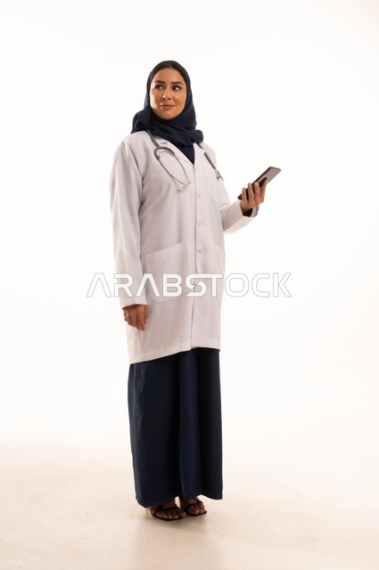 تعابير وايماءات الاندماج والسرور، استخدام التقنية الحديثه المتطورة في الحياة العملية، بورتريه لإمرأة عربية خليجية سعودية ترتدي الحجاب والعباءة تقوم بالعمل على الهاتف المحمول، متابعة وتصفح مواقع التواصل الاجتماعي، صورة الجسم بالطول الكامل، خلفية بيضاء