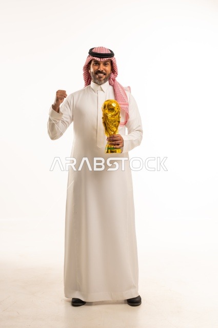 ايماءات السعادة والفرح, مفهوم الربح والفوز، بورتريه لرجل عربي خليجي سعودي يرتدي الثوب التقليدي والشماغ  يحمل بيده كأس العالم الذهبي لرياضة كرة القدم، نشاط بدني للمحافظة على صحة الاجسام و اللياقة، الجسم بالطول الكامل، خلفية بيضاء