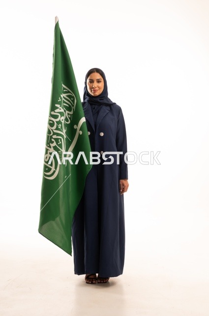 Raising the banner of monotheism and Islam, commemorating the Saudi National Day on September 23, looking with expressions of joy and pride, pride in belonging to the homeland, Flag Day on March 11, a portrait of a smiling Saudi Gulf Arab woman wearing a hijab and an abaya holding the Kingdom's flag in her hand, full-body, white background.