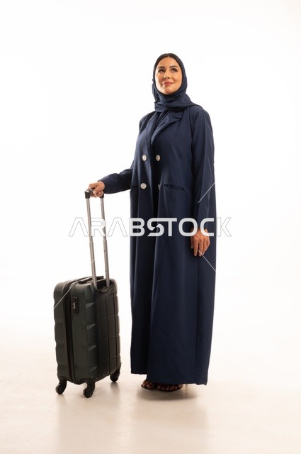Spending an enjoyable summer trip, preparing to start the vacation abroad, gestures of joy and happiness, tourism during the summer holiday, a portrait of a Saudi Arabian Gulf woman wearing a hijab and a coat holding a travel bag in her hand, full-body, white background.