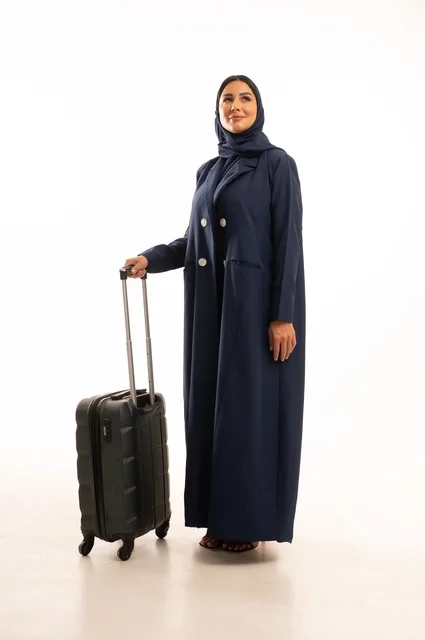 قضاء رحلة صيفية ممتعة, الاستعداد لبدء العطلة خارج البلاد , ايماءات السرور والسعادة، السياحة في إجازة الصيف, بورتريه لامرأة عربية خليجية سعودية محجبة ترتدي البالطو تمسك بيدها حقيبة السفر، الجسم بالطول الكامل, خلفية بيضاء