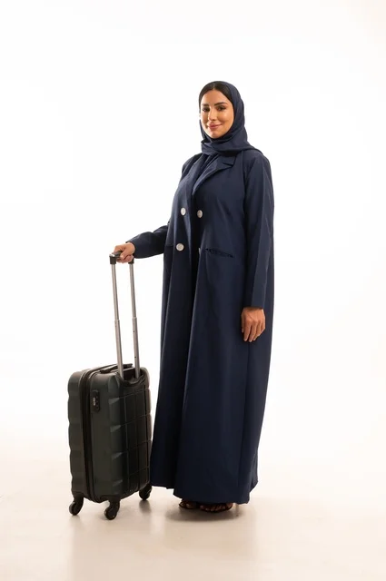 Spending an enjoyable summer trip, preparing to start the vacation abroad, gestures of joy and happiness, tourism during the summer holiday, a portrait of a Saudi Arabian Gulf woman wearing a hijab and a coat holding a travel bag in her hand, full-body, white background.