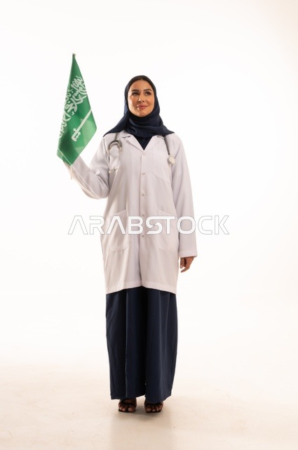 Providing health services to patients, commemorating Saudi National Day on September 23, the concept of medicine and healthcare, a portrait of a Saudi Gulf Arab female doctor wearing a hijab, a coat, and a stethoscope holding the Kingdom's flag in her hand, working in the health sector in the Kingdom, full-body, white background.
