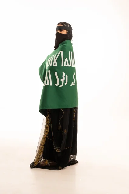 The anniversary of the day we began in 1727 AD, the establishment of the first Saudi state on February 22, wearing the traditional attire of the central region during popular and national occasions, a portrait of a Saudi Gulf Arab woman wearing a burqa and shayla holding the flag and emblem of the Foundation Day with expressions of pride and honor, full-body, white background.