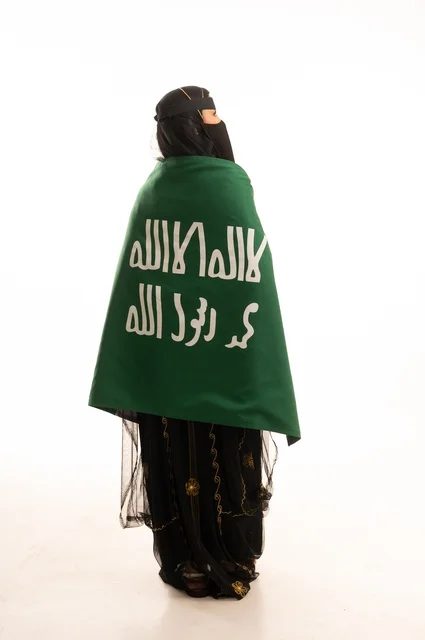 ذكرى يوم بدينا 1727 م، تأسيس الدولة السعودية الأولى 22 فبراير، ارتداء زي المنطقة الوسطى في المناسبات الشعبية والوطنية, بورتريه لإمرأة عربية خليجية سعودية ترتدي البرقع والشيلة تمسك راية وشعار يوم التأسيس بتعابير الفخر والاعتزاز, الجسم بالطول الكامل, خلفية بيضاء