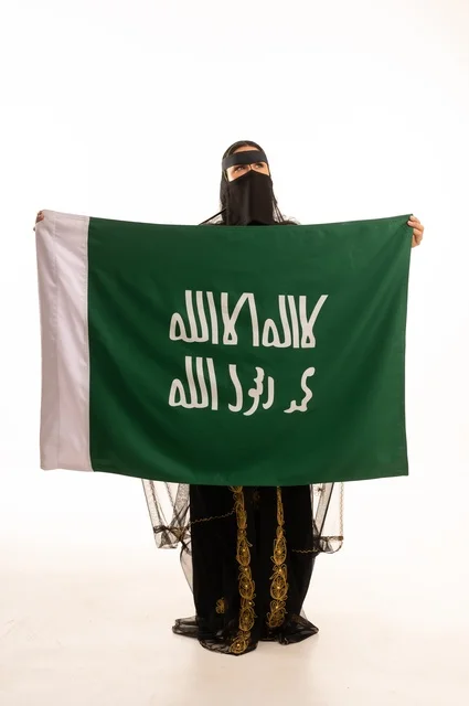 تأسيس الدولة السعودية الأولى 22 فبراير، ذكرى يوم بدينا 1727 م، ارتداء زي المنطقة الوسطى في المناسبات الشعبية والوطنية, بورتريه لإمرأة عربية خليجية سعودية ترتدي البرقع والشيلة تمسك راية وشعار يوم التأسيس بتعابير الفخر والاعتزاز, الجسم بالطول الكامل, خلفية بيضاء