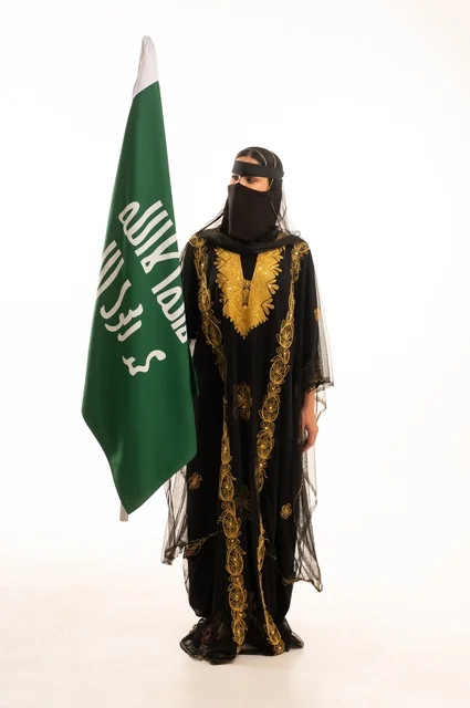 تأسيس الدولة السعودية الأولى 22 فبراير، ذكرى يوم بدينا 1727 م، ارتداء زي المنطقة الوسطى في المناسبات الشعبية والوطنية, بورتريه لإمرأة عربية خليجية سعودية ترتدي البرقع والشيلة تمسك راية وشعار يوم التأسيس بتعابير الفخر والاعتزاز, الجسم بالطول الكامل, خلفية بيضاء