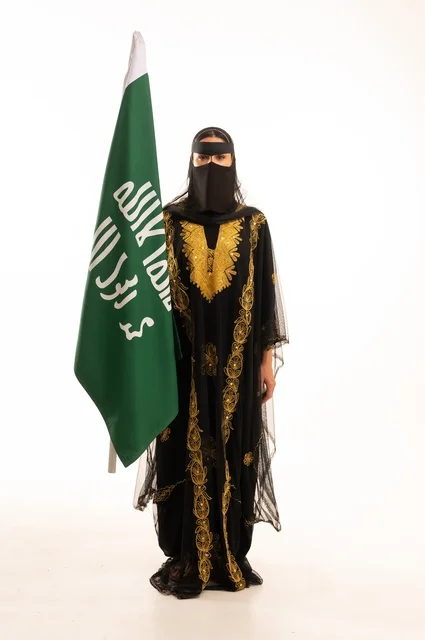 تأسيس الدولة السعودية الأولى 22 فبراير، ذكرى يوم بدينا 1727 م، ارتداء زي المنطقة الوسطى في المناسبات الشعبية والوطنية, بورتريه لإمرأة عربية خليجية سعودية ترتدي البرقع والشيلة تمسك راية وشعار يوم التأسيس بتعابير الفخر والاعتزاز, الجسم بالطول الكامل, خلفية بيضاء