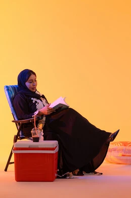 قضاء وقت ممتع في فصل الصيف, مفهوم القراءه والثقافة ، شرب المشروبات الصيفية المنعشة ، بورتريه لامراه عربيه خليجيه اماراتيه ترتدي العباءه المطرزة والحجاب تجلس على كرسي , سيدة سعودية تمسك بيدها كتاب ،  خلفية صفراء