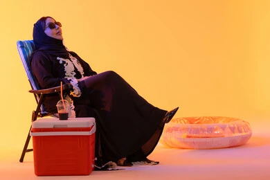 بورتريه لامراه عربيه خليجيه اماراتيه ترتدي العباءه المطرزة والحجاب تجلس على كرسي , قضاء وقت ممتع في فصل الصيف, شرب المشروبات الصيفية المنعشة ،سيدة سعودية تمسك بيدها حافظة البرودة،  خلفية صفراء