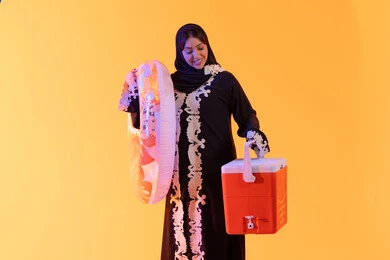 A Saudi woman holding a cooler, enjoying time in the summer, a portrait of an Arab Gulf Emirati woman wearing an embroidered abaya, hijab, and float ready for swimming at the beach, yellow background.