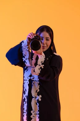 مفهوم إحتراف التصوير  ، بورتريه لامراه عربيه خليجيه اماراتيه تحمل بيدها كاميرا تصوير عالية الدقة ، سيدة سعودية تمارس الهوايات المفضله ،إلتقاط الصور التذكارية ،كاميرا عالية الدقة ،مصوره اماراتيه ، خلفية صفراء