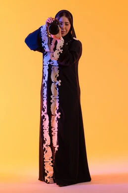 A Saudi woman practicing her favorite hobbies, taking commemorative photos, a high-resolution camera, the concept of professional photography, a portrait of an Arab Gulf Emirati woman holding a high-resolution camera in her hand, an Emirati photographer, with a yellow background.