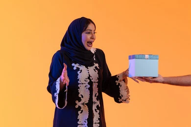 بورتريه مقرب ليد رجل عربي خليجي اماراتي يقوم بتقديم الهدية لزوجته بمناسبة عيد الحب, الألفة والمودة بين الزوجان, مفهوم تقديم الهداية في الاعياد والمناسبات,خلفية صفراء