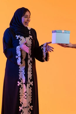 The concept of giving gifts during holidays and occasions, a close-up portrait of the hand of an Emirati Arab man presenting a gift to his wife on the occasion of Valentine's Day, the affection and love between the couple, yellow background.