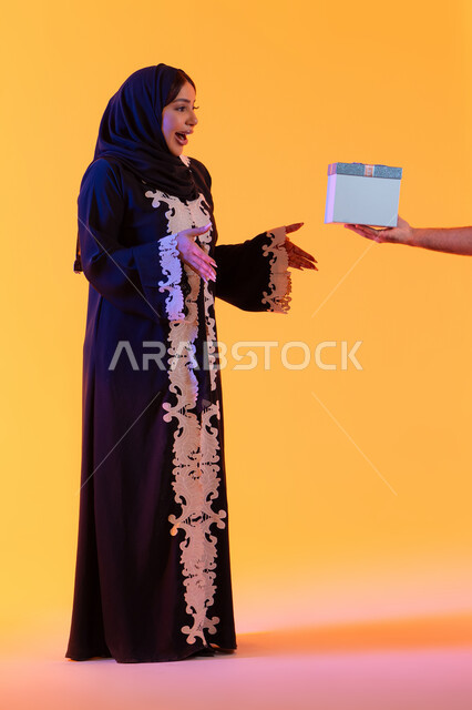 الألفة والمودة بين الزوجان,  مفهوم تقديم الهداية في الاعياد والمناسبات, بورتريه مقرب ليد رجل عربي خليجي اماراتي يقوم بتقديم الهدية لزوجته بمناسبة عيد الحب, خلفية صفراء
