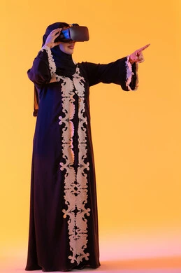 An Emirati woman stands with gestures of integration and interaction with the virtual world, enjoying leisure time through the use of modern electronic technologies. A young Arab Gulf Saudi woman wearing a hijab and an embroidered abaya, she is wearing 3D VR glasses, merging technology with practical life.