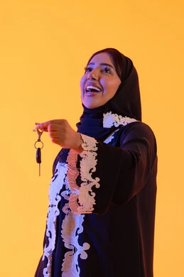 Receiving and delivering the keys, gestures of happiness and joy at owning a new car, a portrait of an Emirati Gulf Arab woman holding the car key in her hand and looking at the camera, a Saudi woman receiving valet parking service in private parking, yellow background. Receiving and delivering the keys, gestures of happiness and joy at owning a new car, a portrait of an Emirati Gulf Arab woman holding the car key in her hand and looking at the camera, a Saudi woman receiving valet parking service in private parking, yellow background.