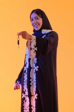 بورتريه لامراه عربيه خليجيه اماراتيه تمسك مفتاح السيارة بيدها وتنظر إلى الكاميرا, سيده سعوديه تحصل على خدمه صف السيارات بالمواقف الخاصه, استلام وتسليم المفاتيح, ايماءات السعاده والسرور بامتلاك سياره جديده, خلفيه صفراء