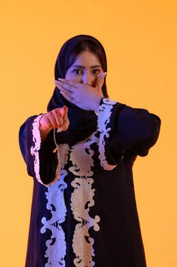 سيدة سعودية تضع يدها على فمها بتعابير المفاجأه، تعابير تشير هذا المكان هنا، تحديد موقع معين ، بورتريه لامراه عربيه خليجيه اماراتيه ترتدي العباءه والحجاب تشير بإصبع السبابة لاعلى إلى شيء ، النظر إلى الكاميرا بإيماءات الفرح والسرور