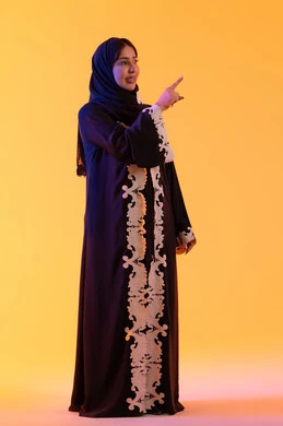 النظر إلى شئ ما بإيماءات الفرح والسرور، تعابير تشير هذا المكان هنا، تحديد موقع معين ، بورتريه لامراه عربيه خليجيه اماراتيه ترتدي العباءه والحجاب تشير بإصبع السبابة لاعلى إلى شيء ،  خلفية صفراء