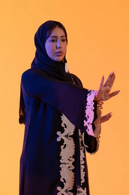 بورتريه مقرب لامراة عربية خليجية إماراتية ترتدي العباءة المطرزة والحجاب تنظر إلى شئ ما، مد اليدين نحو الأمام في محاولة للدفاع عن النفس، مفهوم الخوف والقلق ، سيدة سعودية تشير بترك مسافة أمان وطلب التوقف، خلفية صفراء