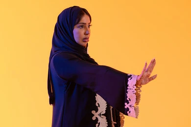 مد اليدين نحو الأمام في محاولة للدفاع عن النفس، مفهوم الخوف والقلق ، بورتريه مقرب لامراة عربية خليجية إماراتية ترتدي العباءة المطرزة والحجاب تنظر إلى الكاميرا، سيدة سعودية تشير بترك مسافة أمان وطلب التوقف، خلفية صفراء