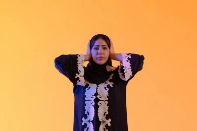 بورتريه لامراه عربيه خليجيه اماراتيه ترتدي العباءه المطرزه والحجاب ترفع يديها على رأسه بتعابير الصدمة والذهول، الانبهار وعدم التصديق, خسارة وفقدان شيء محدد, التفاجؤ والاستغراب من شيء ما, سيده سعوديه تقف بإيماءات التعجب والدهشة، خلفية صفراء