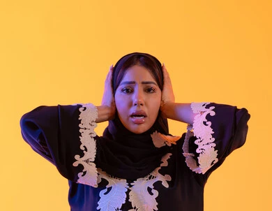 سيده سعوديه تقف بإيماءات التعجب والدهشة، بورتريه لامراه عربيه خليجيه اماراتيه ترتدي العباءه المطرزه والحجاب ترفع يديها على رأسه بتعابير الصدمة والذهول،الانبهار وعدم التصديق, خسارة وفقدان شيء محدد, التفاجؤ والاستغراب من شيء ما,  خلفية صفراء