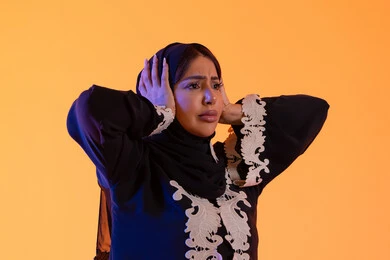 التفاجؤ والاستغراب من شيء ما, الانبهار وعدم التصديق, خسارة وفقدان شيء محدد, سيده سعوديه تقف بإيماءات التعجب والدهشة، بورتريه لامراه عربيه خليجيه اماراتيه ترتدي العباءه المطرزه والحجاب ترفع يديها على رأسه بتعابير الصدمة والذهول، خلفية صفراء