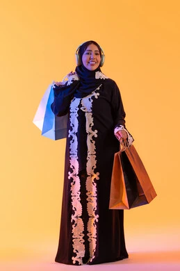 سيدة سعودية تستفيد من العروض الموسمية والتخفيضات، بورترية  لسيده عربية خليجية اماراتيه مبتسمة ترتدي العباءه والحجاب تحمل بيدها أكياس التسوق الملونه، سماع الموسيقي عبر الهيدفون ، التبضع والتسوق من الماركات العالميه، الأثر الإيجابي للتسوق على السيدات،  خلفية صفراء