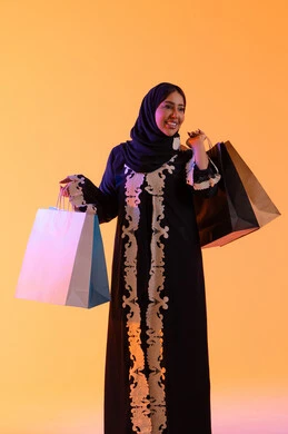 التبضع والتسوق من الماركات العالميه، بورترية لسيده عربية خليجية اماراتيه مبتسمة ترتدي العباءه والحجاب تحمل بيدها أكياس التسوق الملونه، الأثر الإيجابي للتسوق على السيدات، سيدة سعودية تستفيد من العروض الموسمية والتخفيضات،   خلفية صفراء