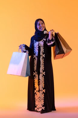 سيدة سعودية تستفيد من العروض الموسمية والتخفيضات،  التبضع والتسوق من الماركات العالميه، بورترية لسيده عربية خليجية اماراتيه مبتسمة ترتدي العباءه والحجاب تحمل بيدها أكياس التسوق الملونه، الأثر الإيجابي للتسوق على السيدات،  خلفية صفراء