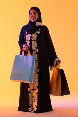 التبضع والتسوق من الماركات العالميه، بورترية لسيده عربية خليجية اماراتيه مبتسمة ترتدي العباءه والحجاب تحمل بيدها أكياس التسوق الملونه، الأثر الإيجابي للتسوق على السيدات، سيدة سعودية تستفيد من العروض الموسمية والتخفيضات،   خلفية صفراء