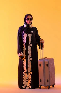 سماع الموسيقي عبر الهيدفون ،ارتداء النظارات الشمسية ، الاستعداد و تجهيز الأمتعة للسفر في جولة سياحية، مفهوم السياحة و السفر، بورتريه لامراه سعوديه مبتسمه تمسك حقيبة سفر ، امراه عربيه خليجيه اماراتيه ترتدي العباءه المطرزة والحجاب تنظر بايماءات وجه تدل على الحماس للقيام برحلة سياحية،  خلفية صفراء