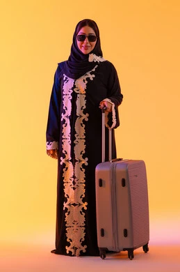 ارتداء النظارات الشمسية ، الاستعداد و تجهيز الأمتعة للسفر في جولة سياحية، مفهوم السياحة و السفر، بورتريه لامراه سعوديه مبتسمه تمسك حقيبة سفر ، امراه عربيه خليجيه اماراتيه ترتدي العباءه المطرزة والحجاب تنظر بايماءات وجه تدل على الحماس للقيام برحلة سياحية،  خلفية صفراء