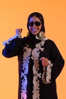 حماية العين باستخدام النظارات الشمسية ،قضاء وقت ممتع بالاستماع الى الموسيقى, مفهوم الإصغاء والاستمتاع، سيدة اماراتية تستخدم الهيدفون في اوقات الفراغ، بورتريه لامرأة عربية خليجية سعودية ترتدي العباءة المطرزة والحجاب تضع سماعات الرأس بتعابير السعادة، تطور التقنيه والتكنولوجيا، خلفية صفراء