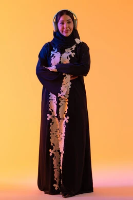 مفهوم الإصغاء والاستمتاع، سيدة اماراتية تستخدم الهيدفون في اوقات الفراغ، بورتريه لامرأة عربية خليجية سعودية ترتدي العباءة المطرزة والحجاب تضع سماعات الرأس بتعابير السعادة، تطور التقنيه والتكنولوجيا، قضاء وقت ممتع بالاستماع الى الموسيقى, خلفية صفراء