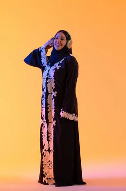 The development of technology and technology, having a good time listening to music, the concept of listening and enjoyment, an Emirati woman using headphones in her free time, a portrait of a Saudi Gulf Arab woman wearing an embroidered abaya and hijab, wearing headphones with expressions of happiness, yellow background.